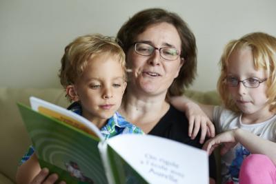 Mor og to børn sidder i sofa. Moren har det ene barn på skødet. De læser en bog.