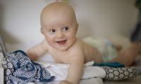 Glad baby med høreapparater ligger på maven på en pusleplads