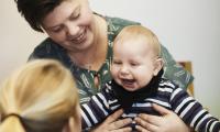 Mor holder en dreng på 6 måneder som smiler til sin AVT-terapeut. 