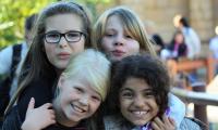 Fire piger på ca. 8-12 år krammer og smiler til fotografen